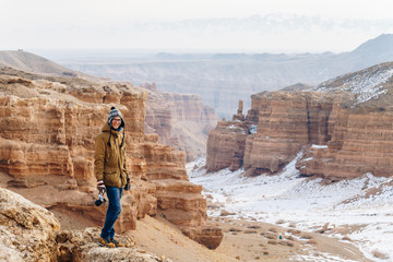 A cheerful traveler with a camera stands on the edge of the cliff in the Charyn canyon in Kazakhstan. Analogue of the American Grand Canyon