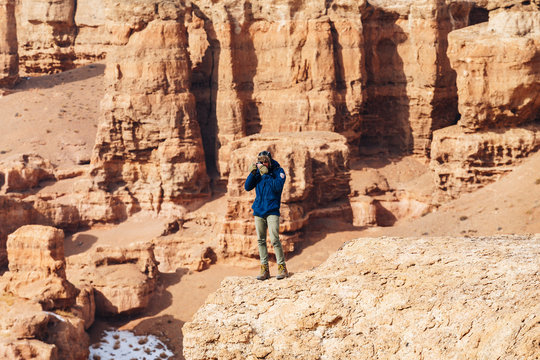 A cheerful traveler with a camera stands on the edge of the cliff in the Charyn canyon in Kazakhstan. 