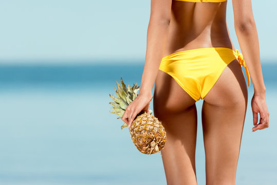 cropped image of woman in bikini holding pineapple in front of sea