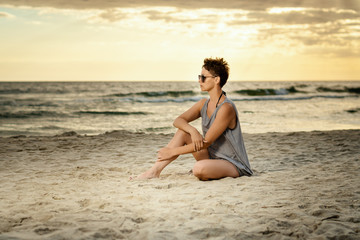 Fototapeta na wymiar beautiful woman in a gray dress sitting on the beach at sunset