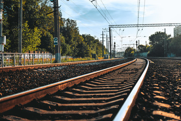 Sunny summer shot of from the ground of railway stretching into the vanishing point; curved railroad track following into distance and bending to the left, with trees, wires, poles, and fence around