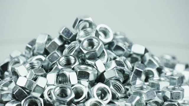 Stack of shiny nuts rotating on a mirror background. Pile of fastener with a threaded hole that forms a connection with a screw, bolt or stud