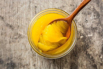 Ghee or clarified butter in jar and wooden spoon on wooden table. Top view