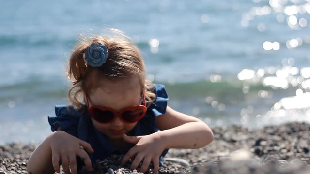 A child play by the sea on a pebble beach on a windy sunny day with glasses in the form of a heart.