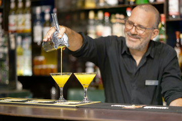 The barman pours an orange cocktail into a glass beaker. The bartender pours the cooked ingredients...