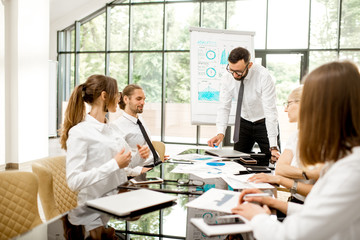 A group of business people strictly dressed in white sitting together during a conference in the spacious office with flip chart on the green background