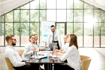 A group of business people strictly dressed in white sitting together during a conference in the spacious office with big window on the background