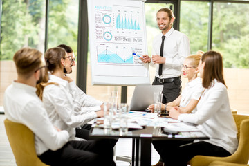 Fototapeta premium Handsome speaker reporting with flip chart during a business conference with partners sitting at the table in the office