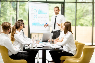 Handsome speaker reporting with flip chart during a business conference with partners sitting at...