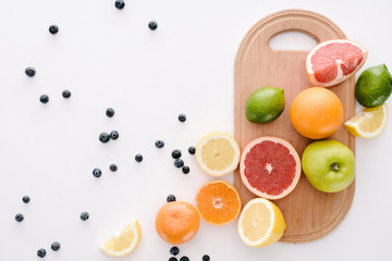 top view of citrus fruits with blueberries and wooden cutting board on white surface