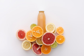 top view of bottle of juice with citrus fruits slices on white surface