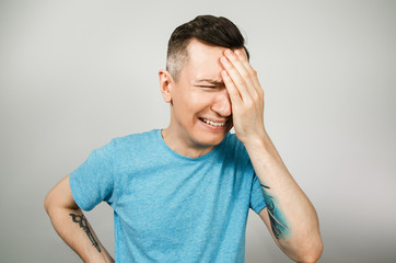 A young guy is crying with hand at face, dressed in a blue T-shirt on a light background.