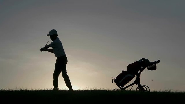 Silhouette of boy golfer with golf bag at sunset