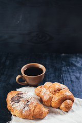 sweet croissants and cup of coffee on black wooden background. Copy space