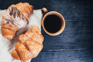 sweet croissants and cup of coffee on black wooden background. Copy space