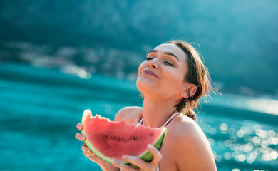 Attractive young woman on the beach eating watermelon