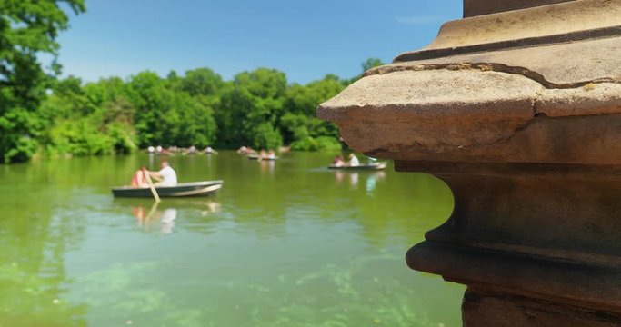A slow dolly reveal establishing shot of unidentifiable tourists in rowboats on The Lake in Central Park. Shallow depth of field.  	