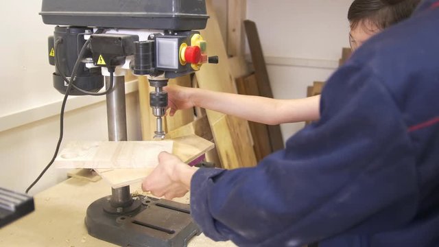 Father and son drills the wooden plank using joinery machine in carpentry workshop