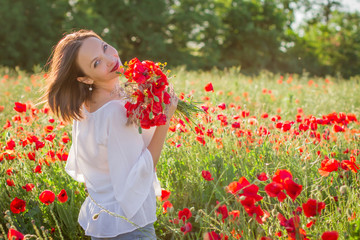 Naklejka premium Woman with bouquet among poppies field at sunset