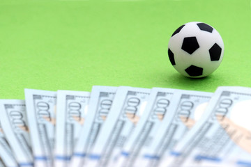 A soccer ball on a green field, next to hundred-dollar bills of the US. Shallow depth of field. Concept money and football, the profits from the fans, the salary of players and coaches, sports betting