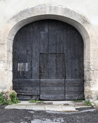 Fototapeta na wymiar very old dark wooden arched door in ancient limestone wall of house in french provence