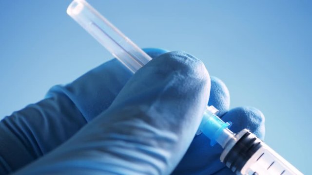 Doctor in blue latex gloves holding syringe and open needle