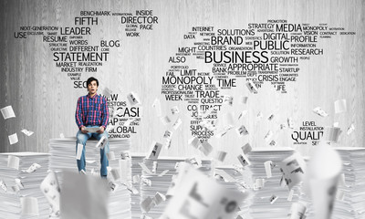 Attractive man sitting on pile of paper documents.