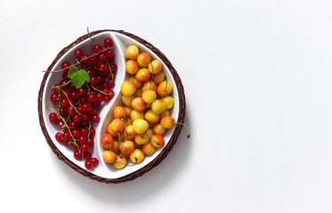 on white background round bowl of yin yang with summer berries of red currant and yellow cherry green leaf