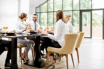 Fototapeta premium Business people dressed in white shirts having fun sitting together during a business lunch with delicious meals and wine in the modern restaurant