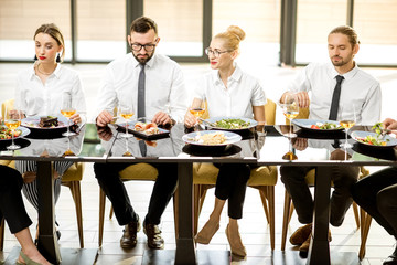 Business people dressed in white shirts having business lunch sitting in a row at the table in the...