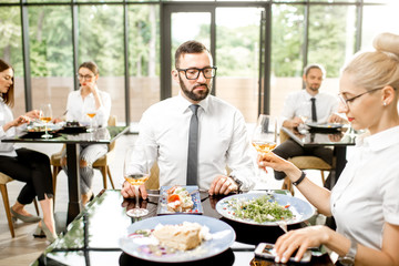 Beautiful couple having business lunch with delicious meals sitting at the modern restaurant with business people on the background