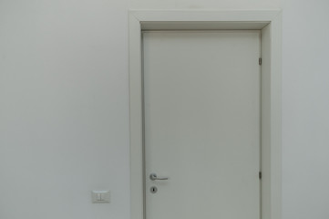 interior white door/White wood finish texture door on a white wall with a white light switch near it.