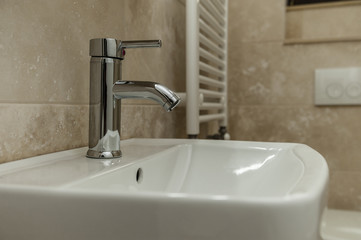 Water faucet/Chrome and shiny water tap faucet in a stylish creamy marble bathroom.