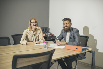 Obraz premium Sensual woman and bearded man smile at business meeting. Happy business woman and man sit at office desk. Concentration at work. Communication and cooperation with colleagues. Work process concept