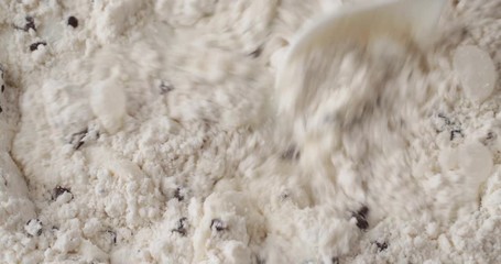 Close video of stirring milk into dry clumpy chocolate chip muffin mix with a white spoon.