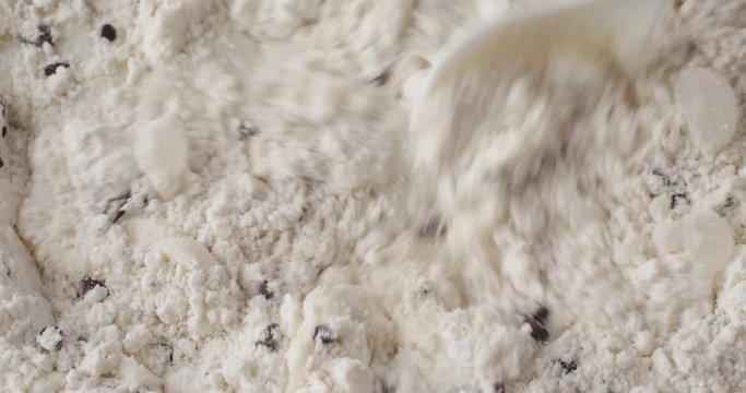 Close video of stirring milk into dry clumpy chocolate chip muffin mix with a white spoon.
