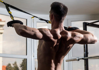 Sportsman, athlete, muscular macho does exercise with trx loops, window on background, close up....