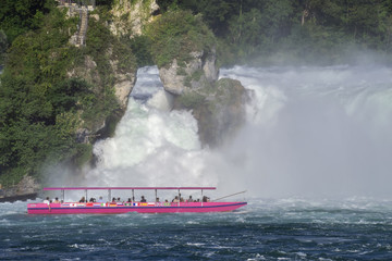 boat with tourists closely pours to the waterfall on the Rhine river in Switzerland, the beauty of Europe