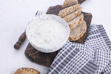 Yoghurt with cucumber. Fresh dip of famous Greek taziki with cucumber. fresh bread, towel and white background. Copy space.