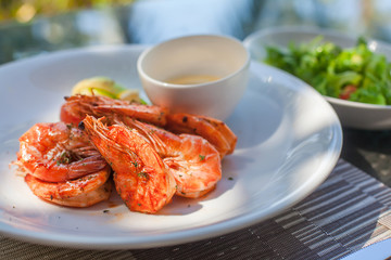 Grilled shrimps on plate with sauce and plate with green salad with tomato. Outdoor photo