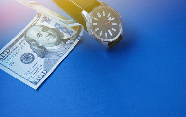 One hundred dollars and a watch on a blue background under the sunlight, top view