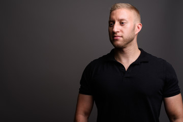 Man with blond hair wearing black polo shirt against gray backgr