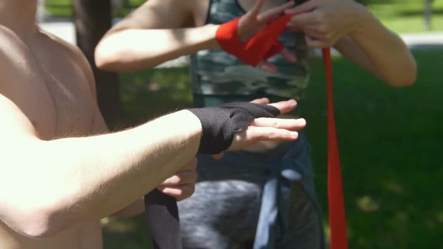 Hands of young man and woman wrapping hands with bandages for workout in summer day