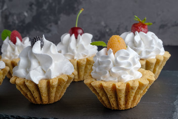 Few cakes with protein cream and berries on dark stone plate on grey background. Close-up view, selective focus