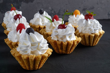 Group of cakes with protein cream and berries on dark stone plate on grey background. Close-up view, selective focus. Copy space for text