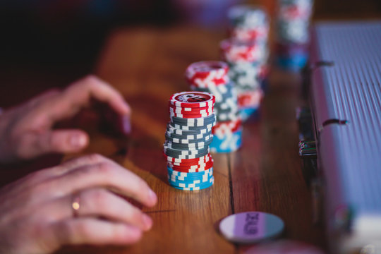 A close-up vibrant image of multicolored casino table with roulette in motion, with the hand of croupier, and a group of gambling rich wealthy people in the background
