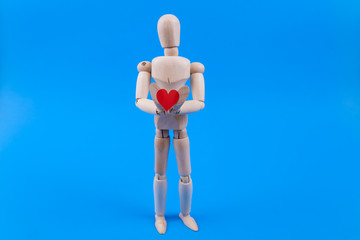 Holding a heart one wooden manikin figure on solid blue background