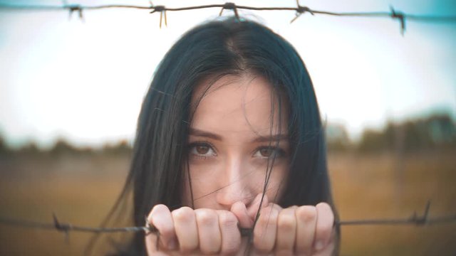 girl brunette refugee behind barbed wire camp slow motion lifestyle video. the concept of freedom is upset Woman hands and barbed wire. girl Refugee, prison, refugees captivity concept