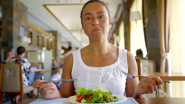 a young woman eats a green salad, a lady gently holds a fork and knife