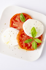 Mozzarella and tomatoes with basil on a white square plate. The background is white. Vertically.
